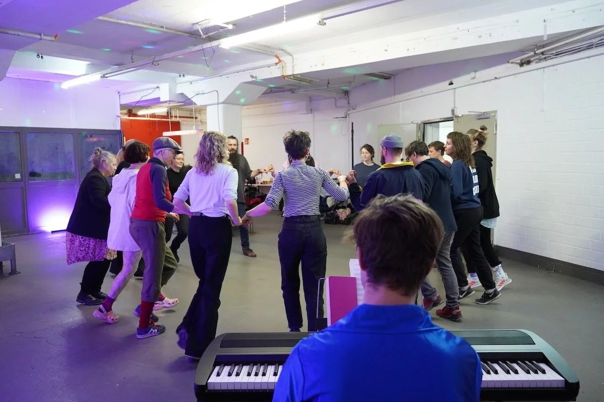 In a rehearsal room, workshop participants try their hand at a crescendo dance. In the foreground, a person sits at a piano.