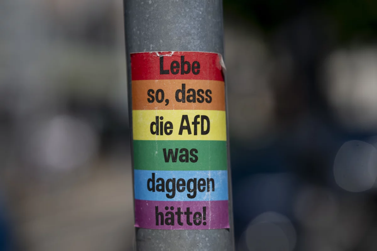 Aufkleber an einem Laternenmast. Aufs Regenbogenfarben steht in schwarzer Schrift: "Lebe so, dass die AfD was dagegen hätte!"