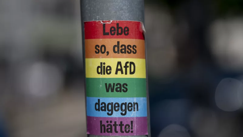 Aufkleber an einem Laternenmast. Aufs Regenbogenfarben steht in schwarzer Schrift: "Lebe so, dass die AfD was dagegen hätte!"