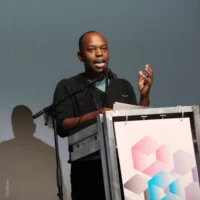 The picture shows Ogutu Muraya standing at the lectern. He gives his impulse speech in front of the audience.