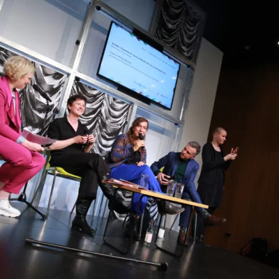 The picture shows four people sitting next to each other on stage. They are discussing with each other as part of a panel discussion.