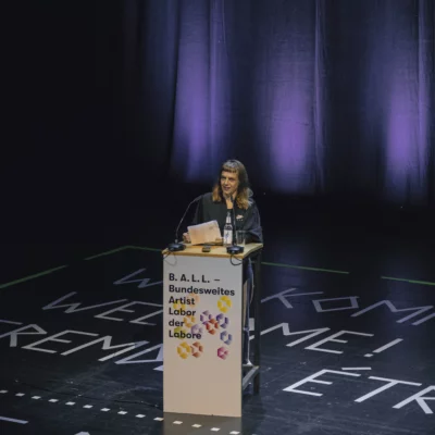 Eine Frau steht auf einer Theaterbühne am Pult.