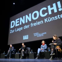 Podiumsgespräch nach der Filmvorführung mit Gästen aus Politik und Kunst. Sie sitzen in einer Stuhlreihe auf der Bühne, über ihnen ist eine Projektion mit dem Titel des Films zu sehen.