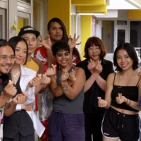 Group picture with ten artists in the context of an Artist Lab. Standing in a semicircle, they look into the camera, their hands snapping their fingers.