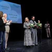 The award winners Hofmann and Lindholm with flowers in their hands in the middle of the stage. To the side of them, the speakers applaud them.