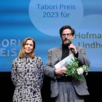 Portrait of the award winners Hofmann and Lindholm, standing in front of the stage screen.