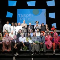 Group photo with the 30 or so participants of the evening on the steps of the HAU1 stage. In the background a large screen with the Tabori Prize lettering.