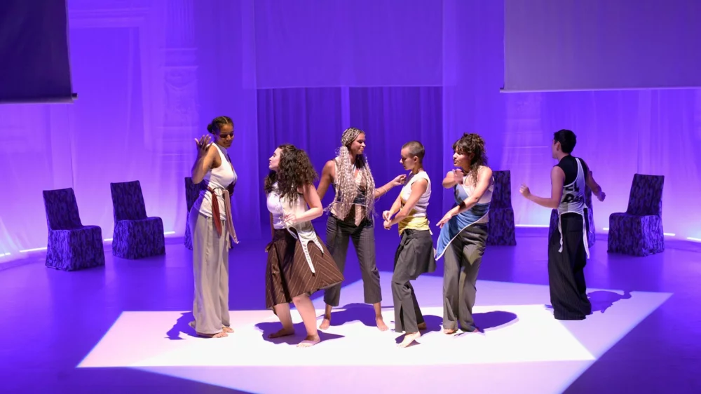 A group of women stand on stage in a rectangular field of light. They each dance for themselves and yet together.