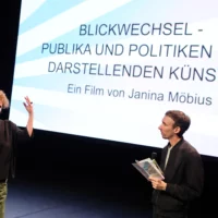 Bühne des HAU3. Auf der Leinwand steht "BLICKWECHSEL - Publika und Politik der Darstellenden Künste". Davor Janina Möbius und Sebastian Köthe.