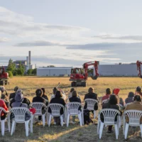 From fully occupied rows of garden chairs in an open field, the audience watches the scene of "Baggern", the performance by Studio Urbanistan, in front of them: three diggers take up position on the wide field in front of industrial plants on the horizon for their further choreography.