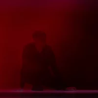 In diffusem, rotem Licht sitzt der Tänzer Viktor Szeri auf der Bühne, in Nebel gehüllt.