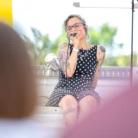 Die Sängerin Sukini sitzt an der Bühnenkante und singt in ein Mikrofon.